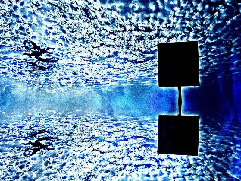 Abstract photograph: a dark angular marker floating in a deep blue field, with a bright band of glare running through the center like a doorway of light.