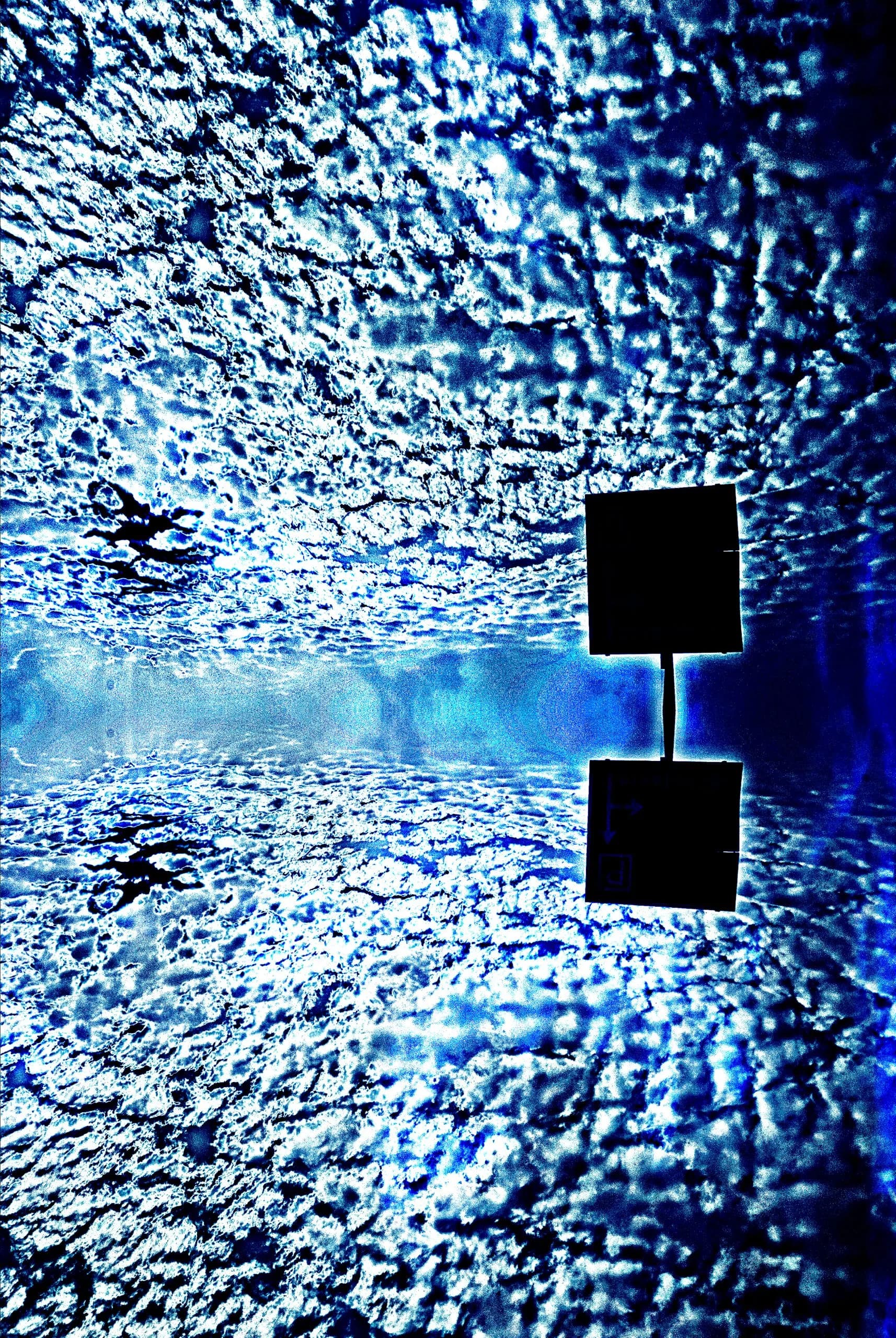 Abstract photograph: a dark angular marker floating in a deep blue field, with a bright band of glare running through the center like a doorway of light.